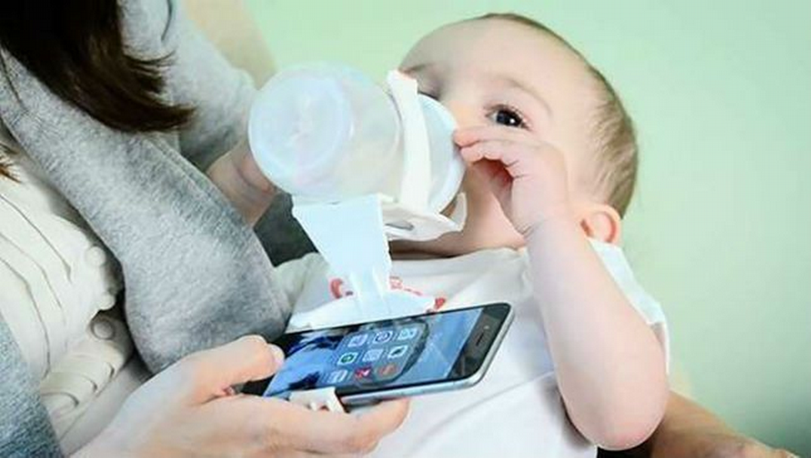 Bébé buvant son biberon et maman sur le télephone